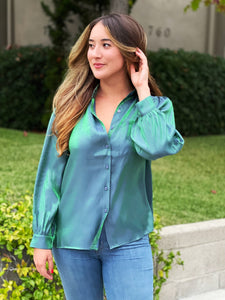 A shiny holographic green blue blouse with buttons and a high-low cut. The fit is loose with puff sleeves.