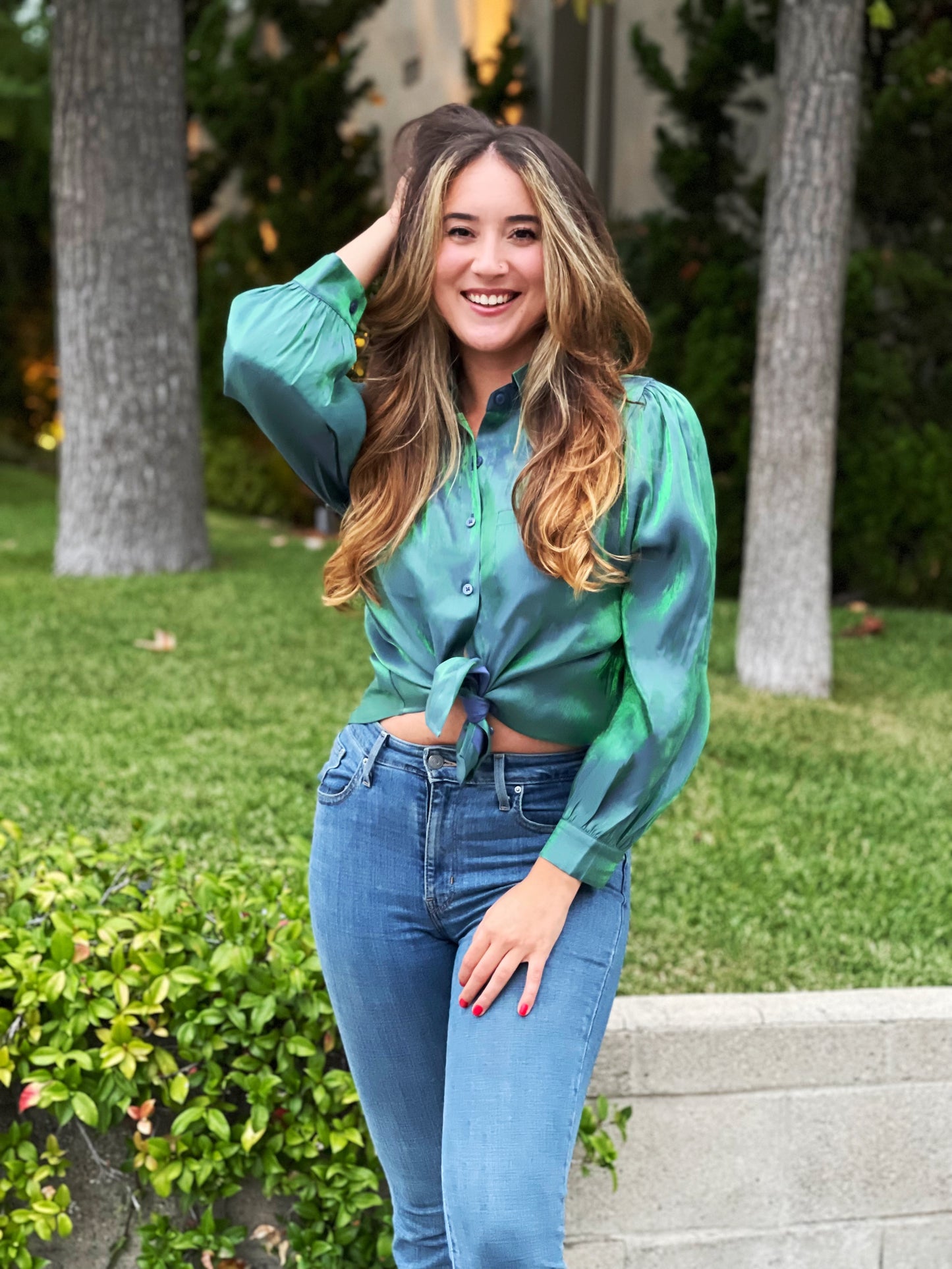 A shiny holographic green blue blouse with buttons and a high-low cut. The fit is loose with puff sleeves.