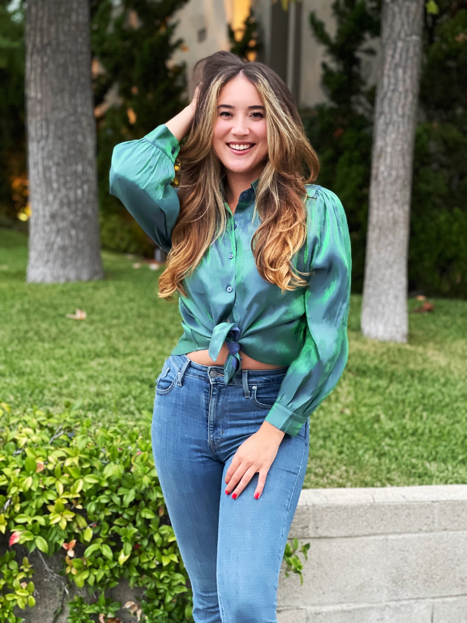 A shiny holographic green blue blouse with buttons and a high-low cut. The fit is loose with puff sleeves.
